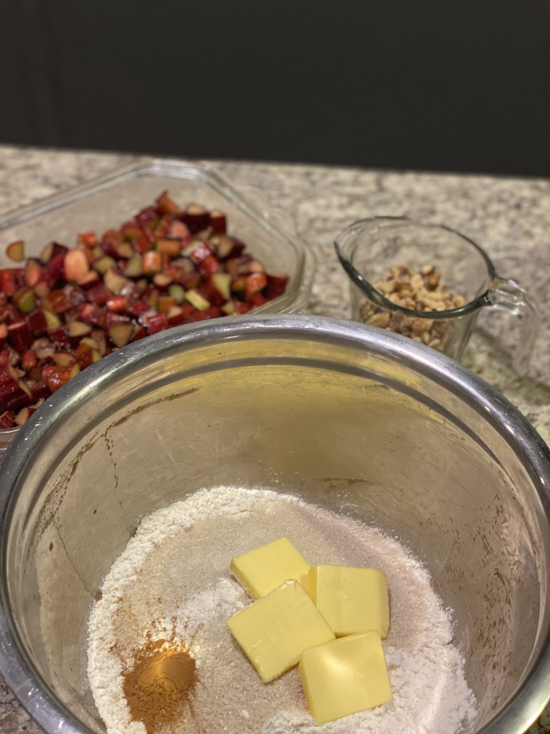 Bowl with flour, butter, and spices on a countertop with other ingredients in the background. Rhubarb & Ginger Crumble