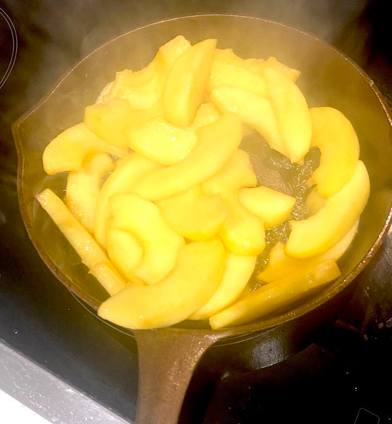 Sliced apples being fried in a cast iron skillet on a stovetop.