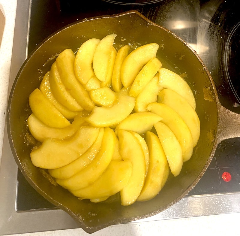 Sliced apples arranged in a spiral pattern in a cast iron skillet on a stovetop.