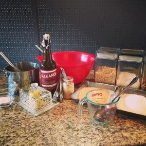 Baking ingredients and utensils on a kitchen counter with a dark backsplash.