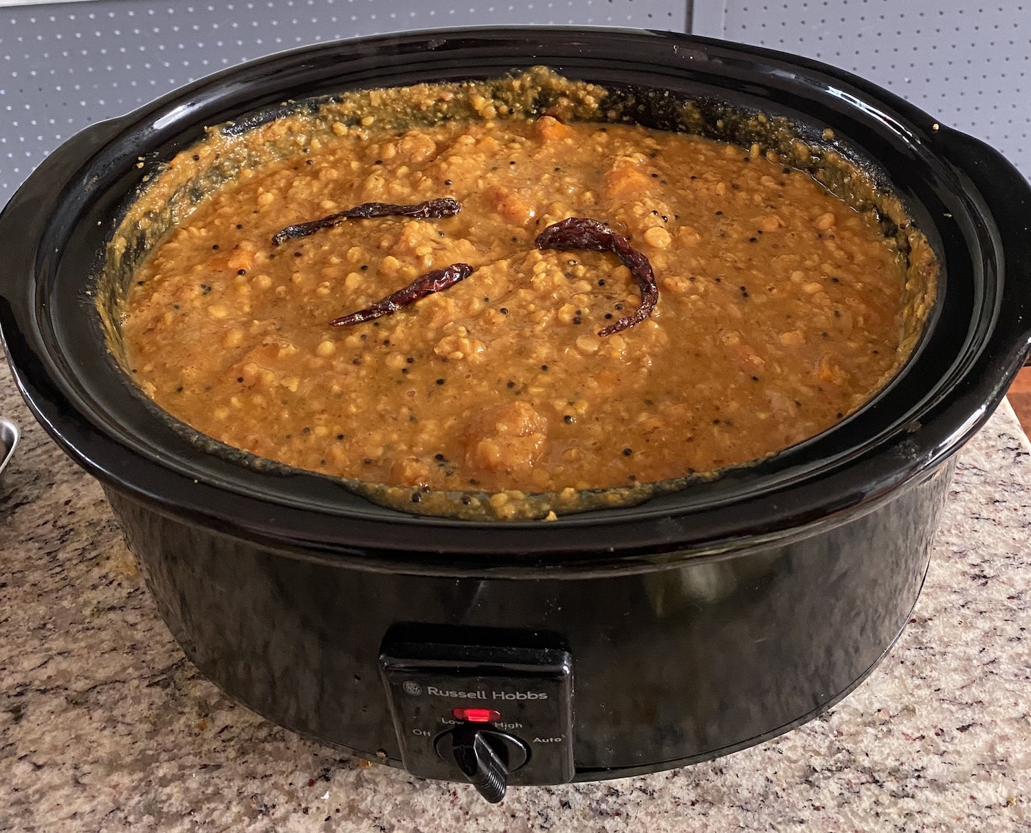 Slow cooker with a dish of lentils  (dhal) and vegetables on a countertop