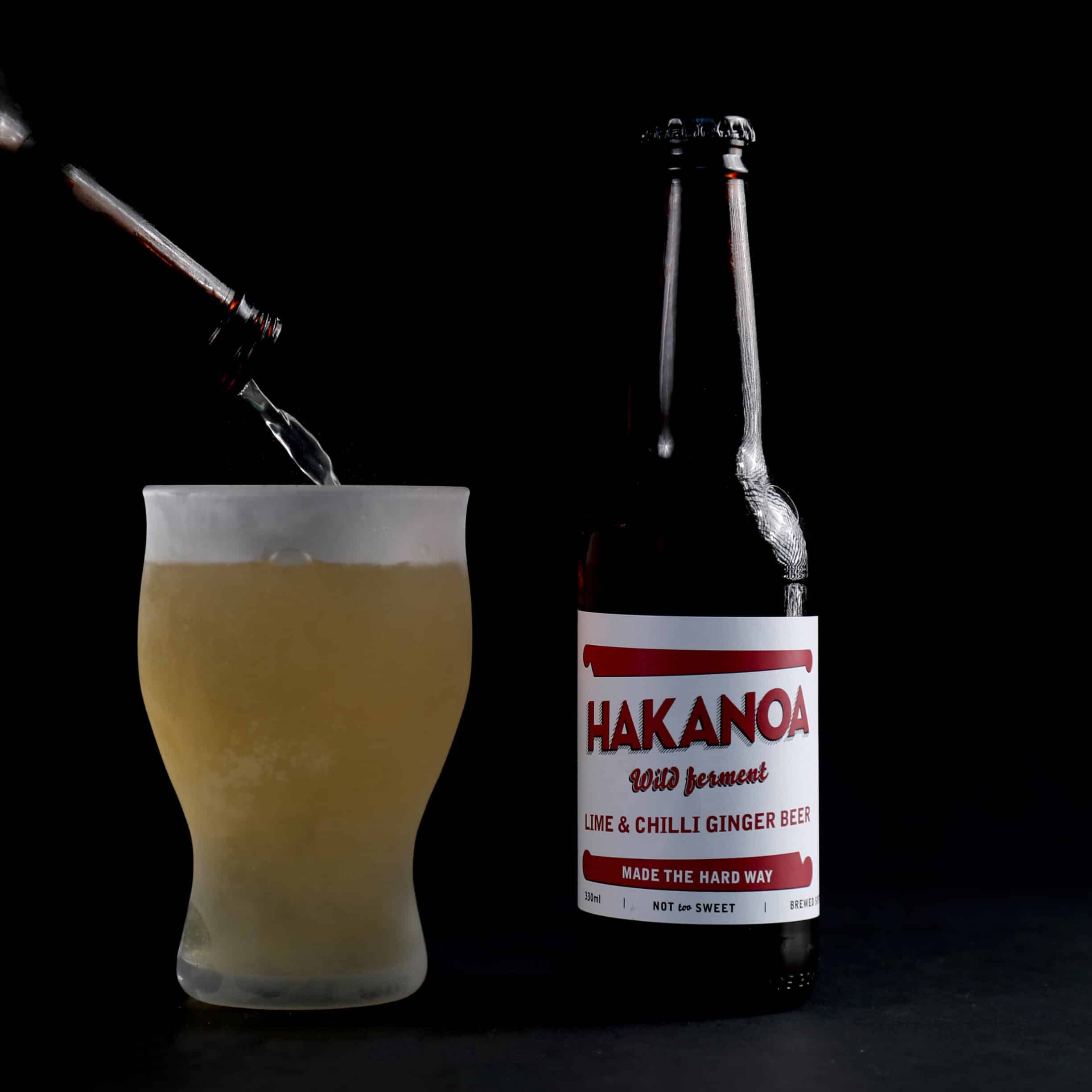Hakanoa ginger beer bottle being poured into a glass on a black background