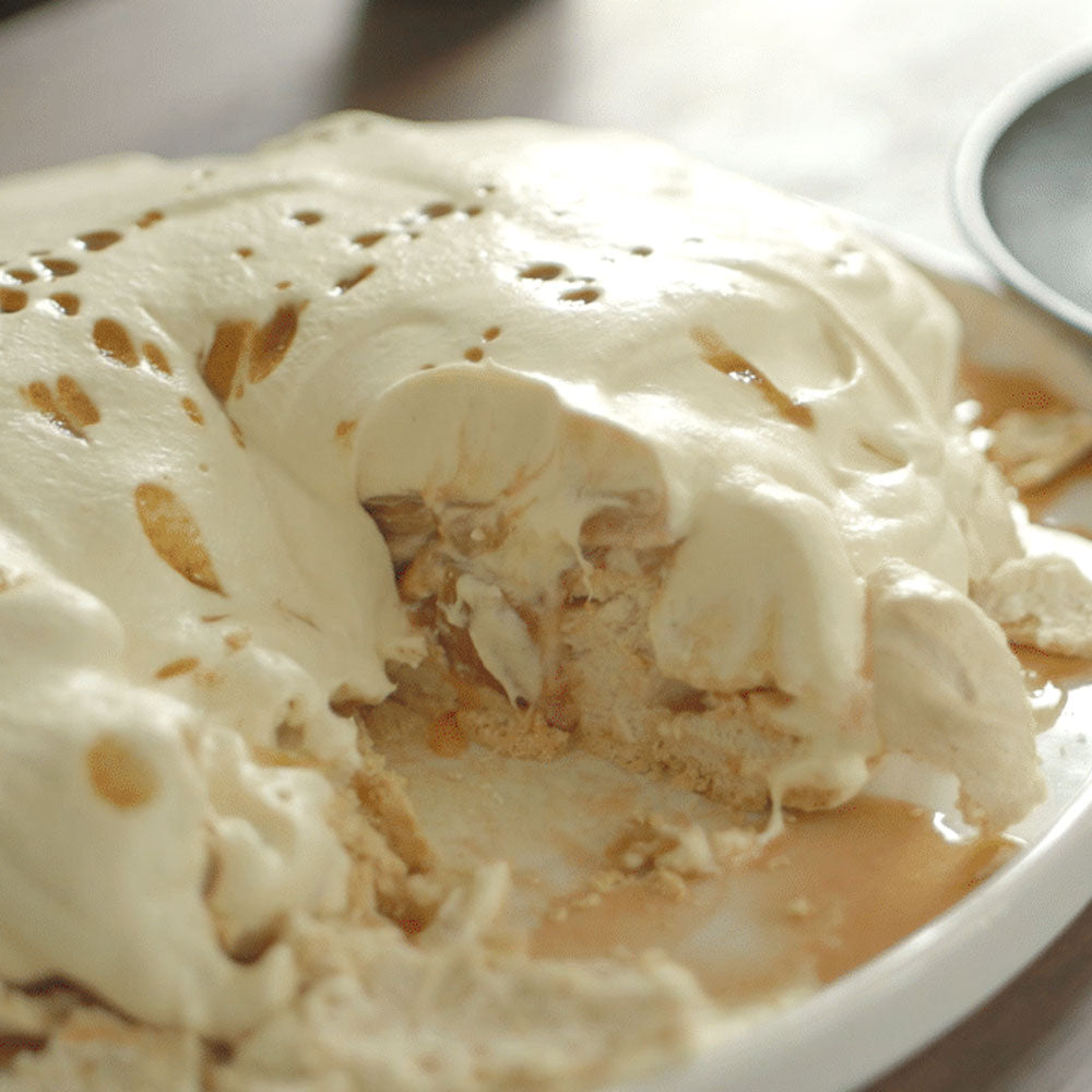 Close-up of a dessert with whipped cream and cookie pieces on a white plate.