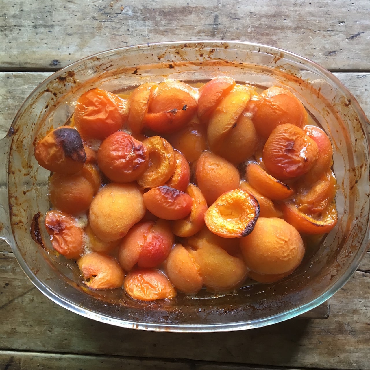 Baked apricots in a glass dish on a wooden surface