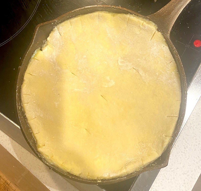Uncooked pie crust in a cast iron skillet on a stovetop.